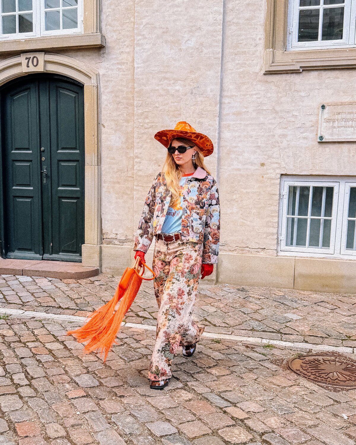 A Copenhagen Fashion Week guest in a patterned outfit with an orange hat and fringed bag