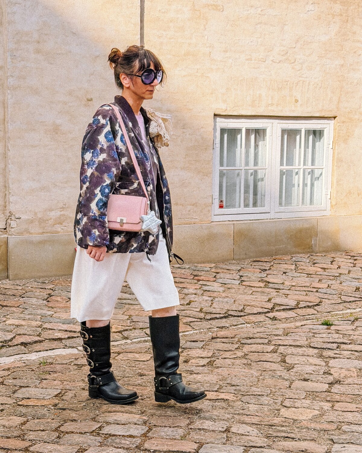 A Copenhagen Fashion Week guest wearing a floral jacket, oversized sunglasses and black boots